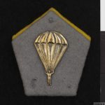 badge, collar, Polish, 1st Polish Independent Parachute Brigade (INS 8082) Pentagonal shaped grey cloth badge. Fixed to the badge is a silver metal parachute and paratrooper. Copyright: © IWM. Original Source: http://www.iwm.org.uk/collections/item/object/30080311